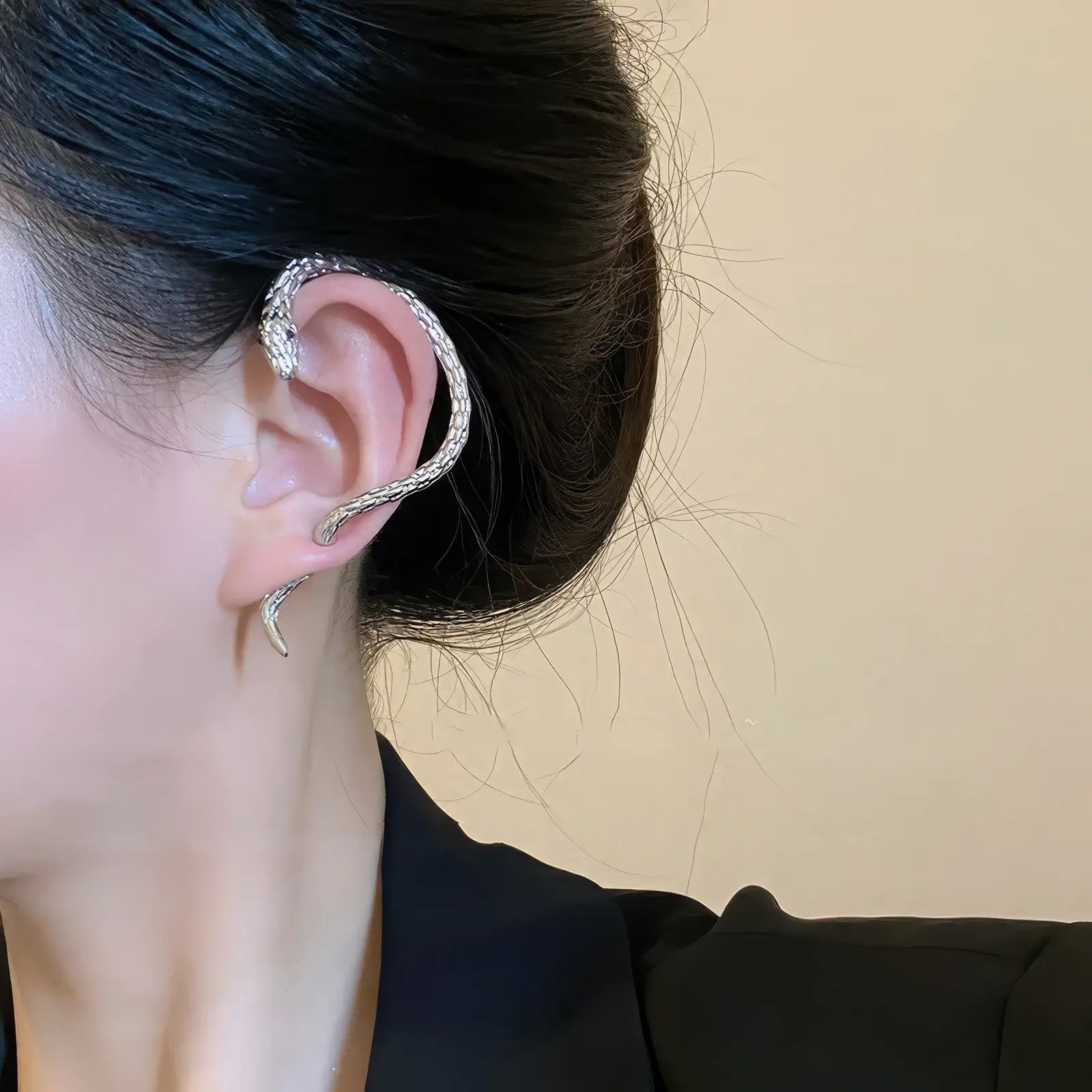 Silver snake - shaped ear cuff worn on the left ear, highlighting the stylish, coiled snake appearance.