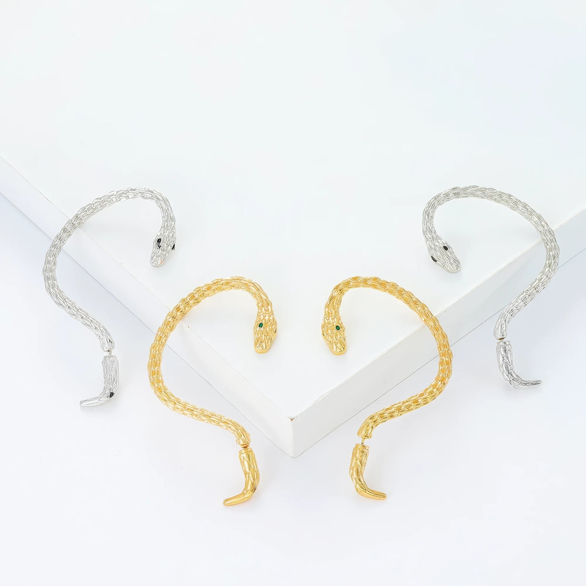 Mixed silver and gold snake - shaped ear cuffs, displayed on white surface, showcasing the variety of metallic tones.