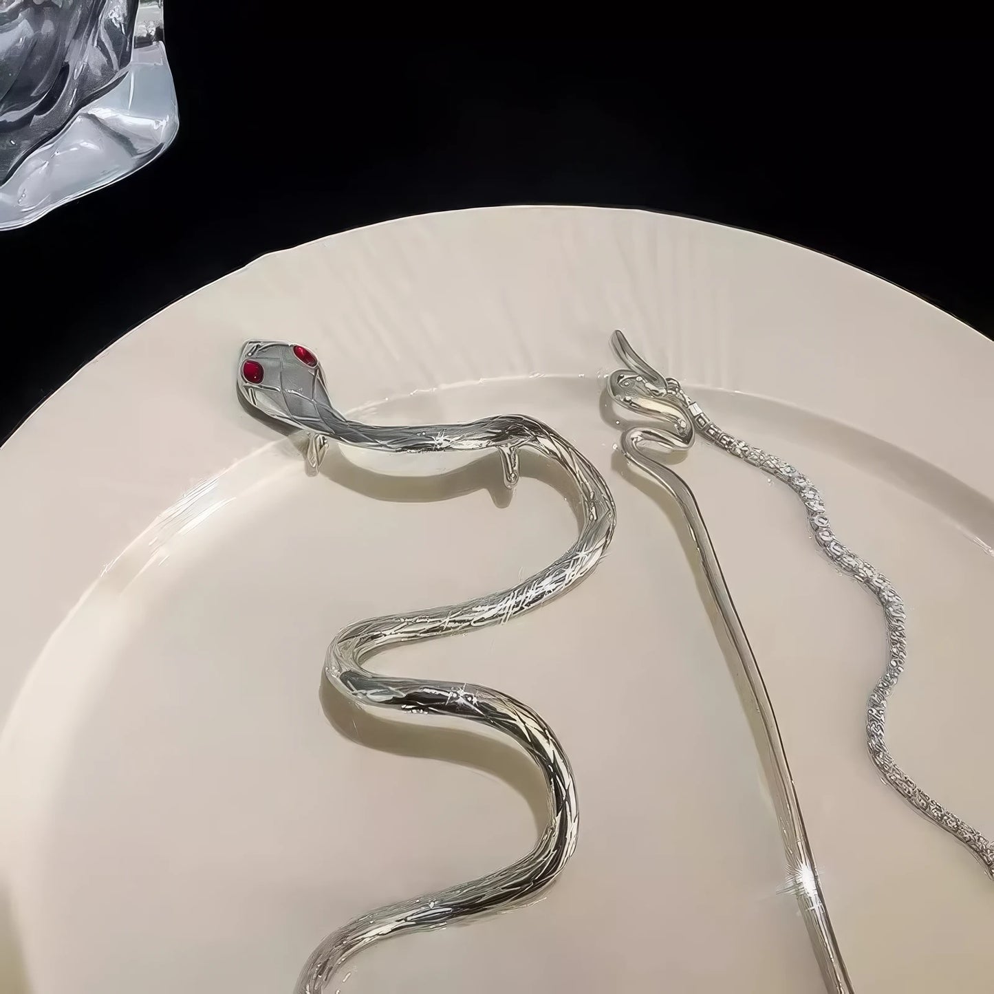 Two silver snake tassel hairpins on a white plate, highlighting the red-eyed snake head and sparkling stone details clearly.
