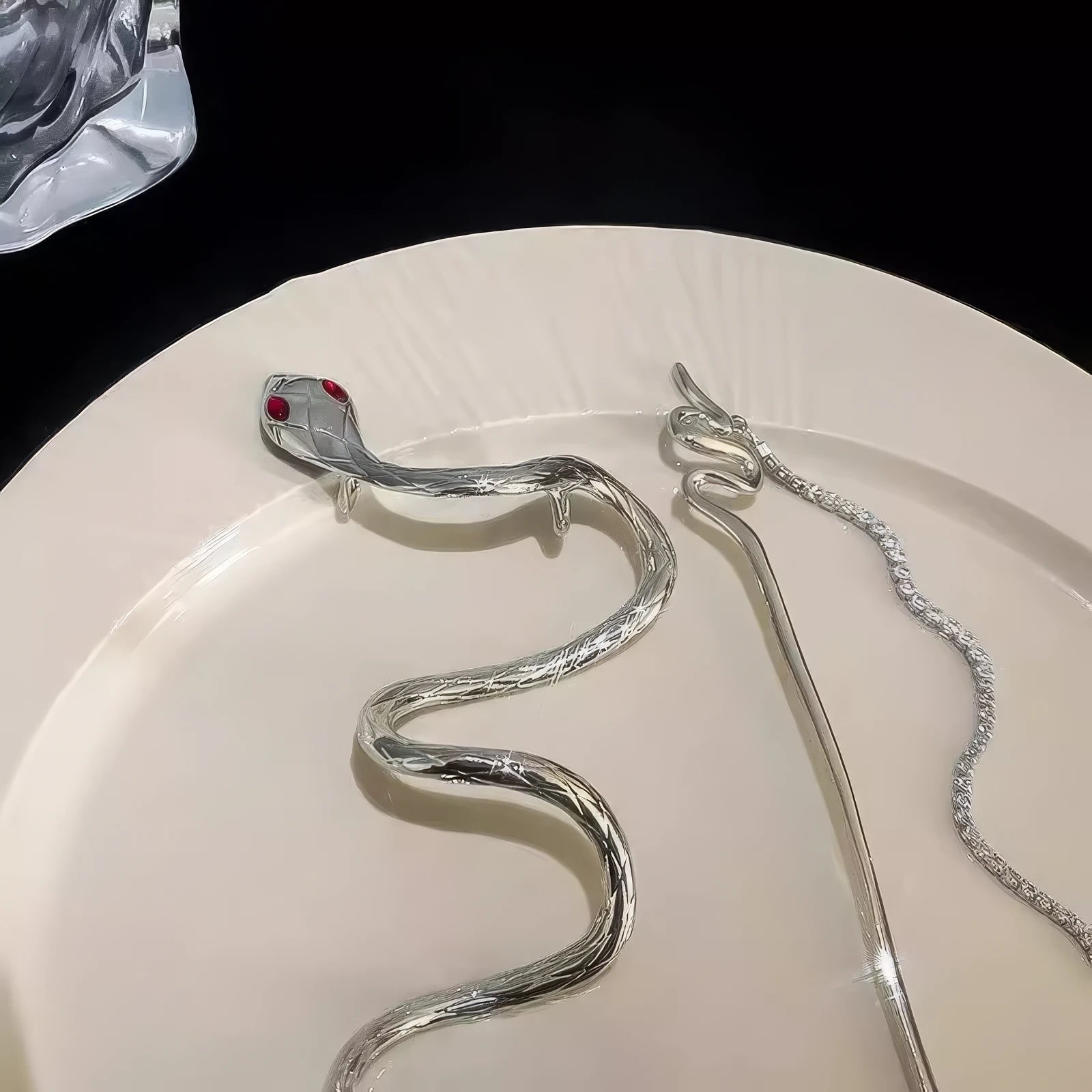 Two silver snake tassel hairpins on a white plate, highlighting the red-eyed snake head and sparkling stone details clearly.