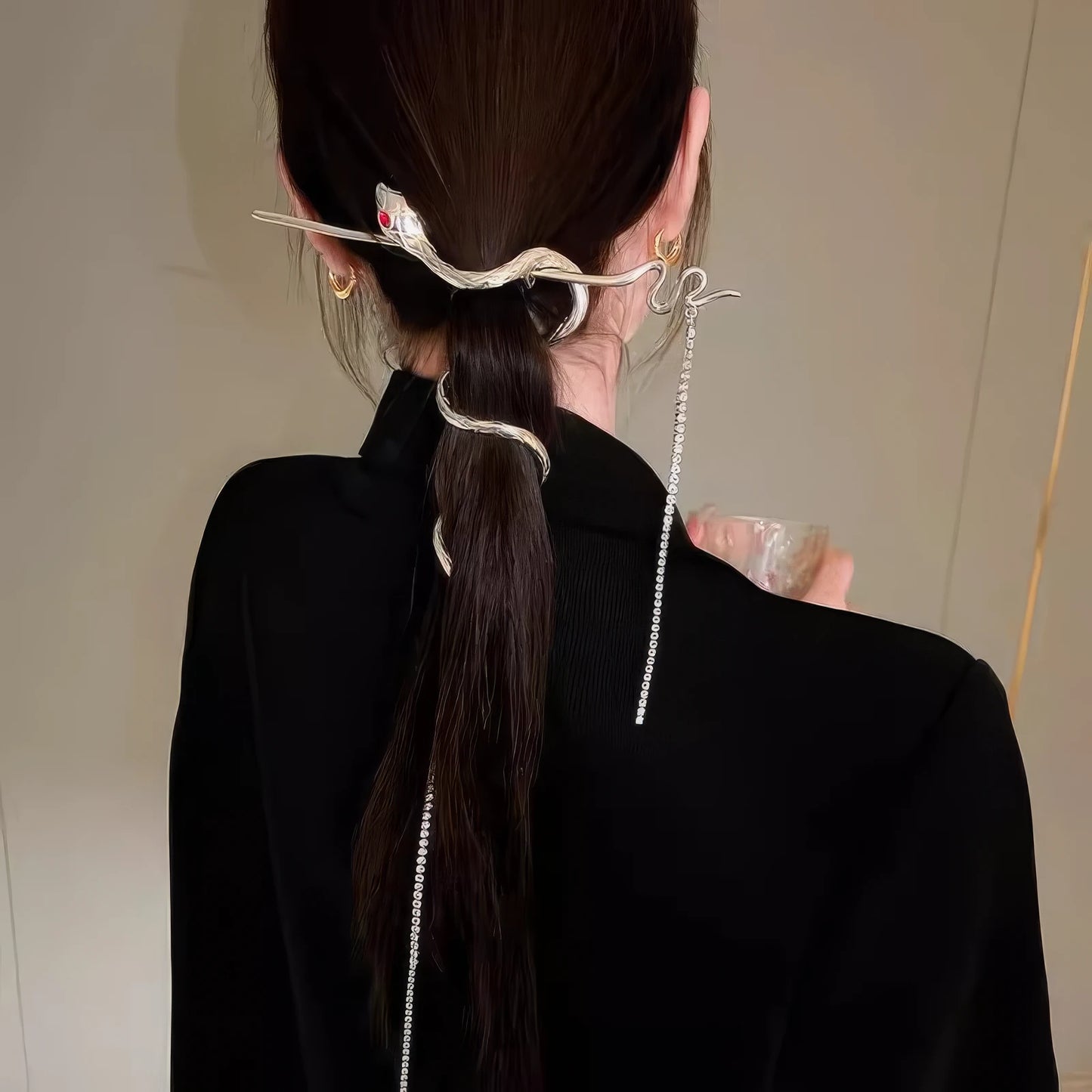 A woman in black outfit wearing a snake tassel hairpin to secure her low ponytail, with the extra-long tassel hanging down the back for an edgy look.