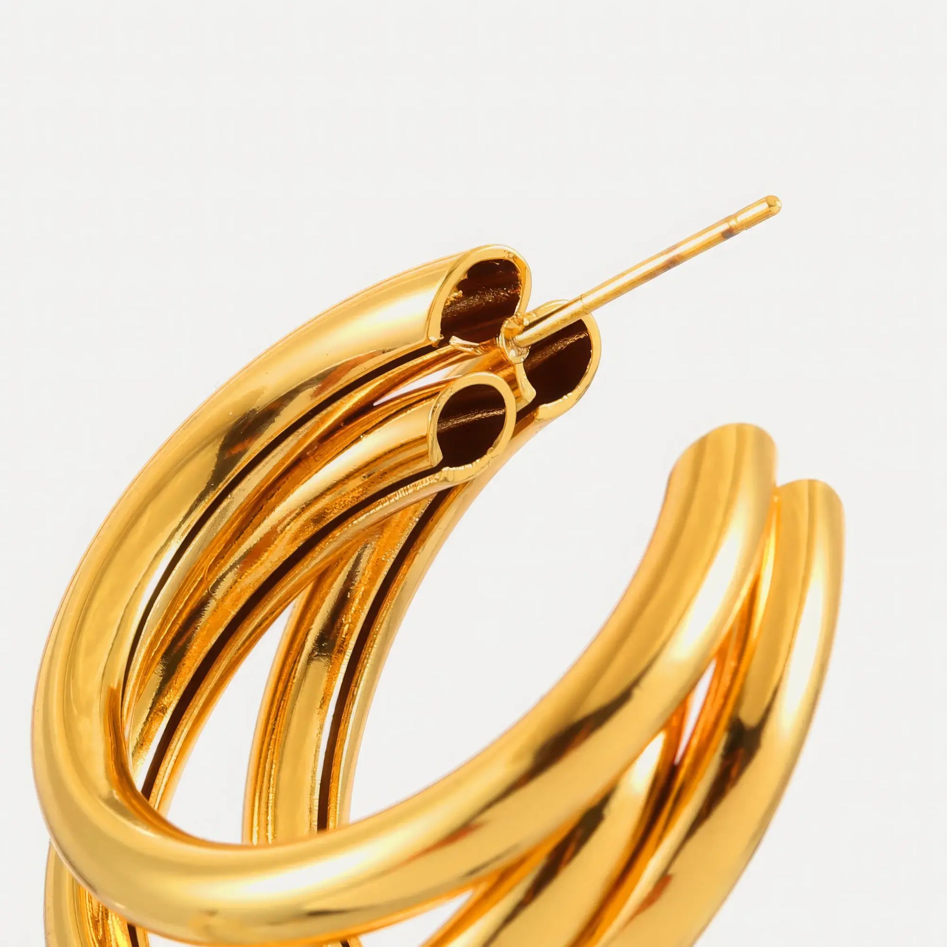 Close - up of gold unique - shaped hoop earring, highlighting the multi - layered, curved structure