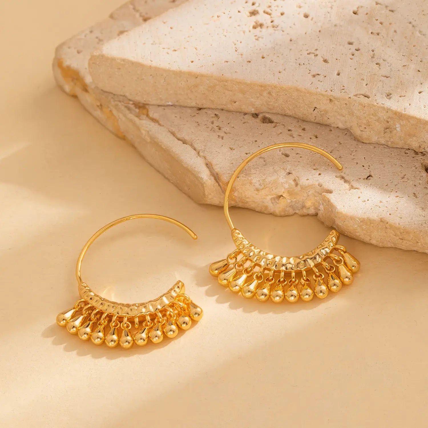 Pair of gold water drop tassel earrings, displayed on a textured surface, highlighting the elegant, dangling water drop structure