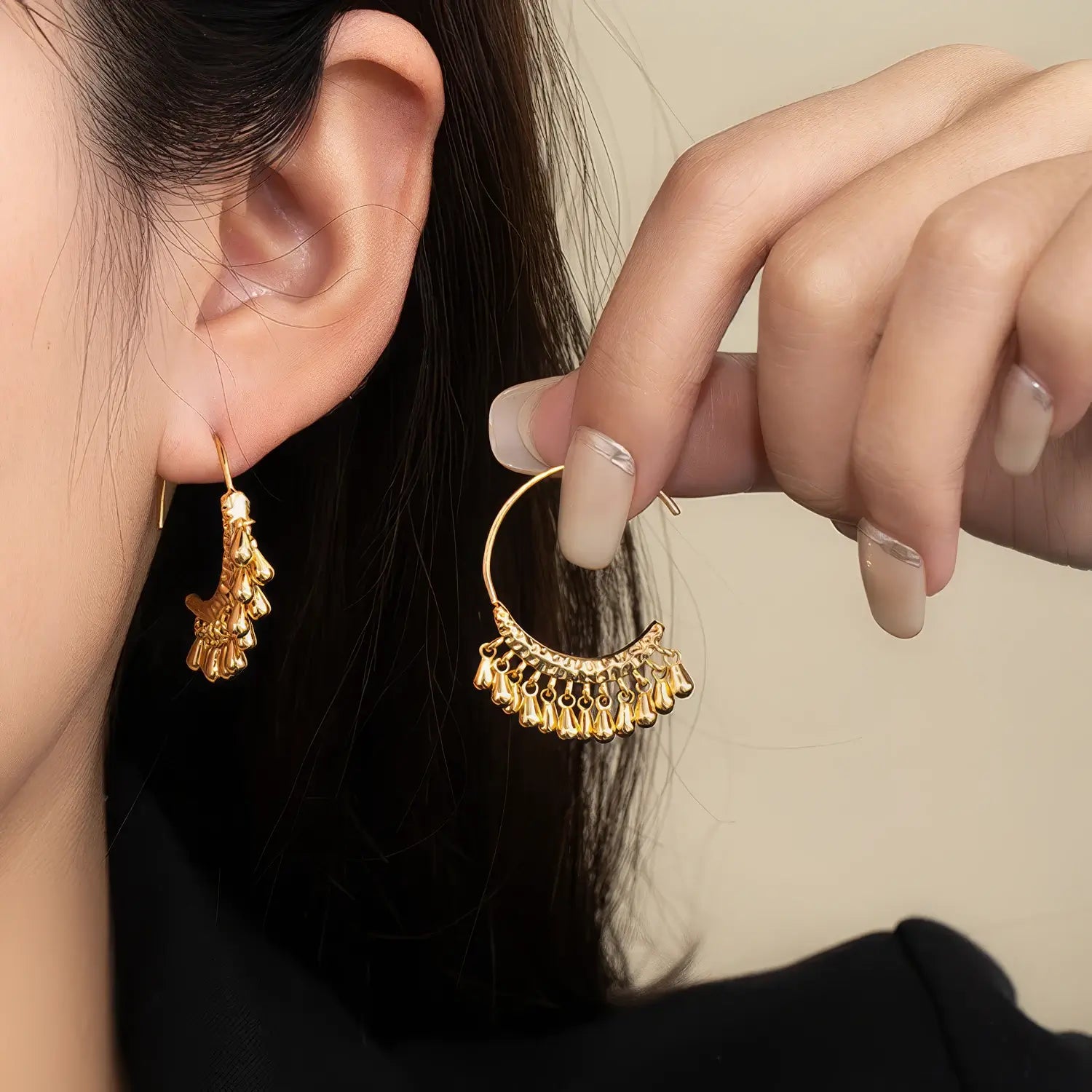 Gold water drop tassel earring worn, with hand holding the other earring, highlighting the elegant, dangling water drop structure