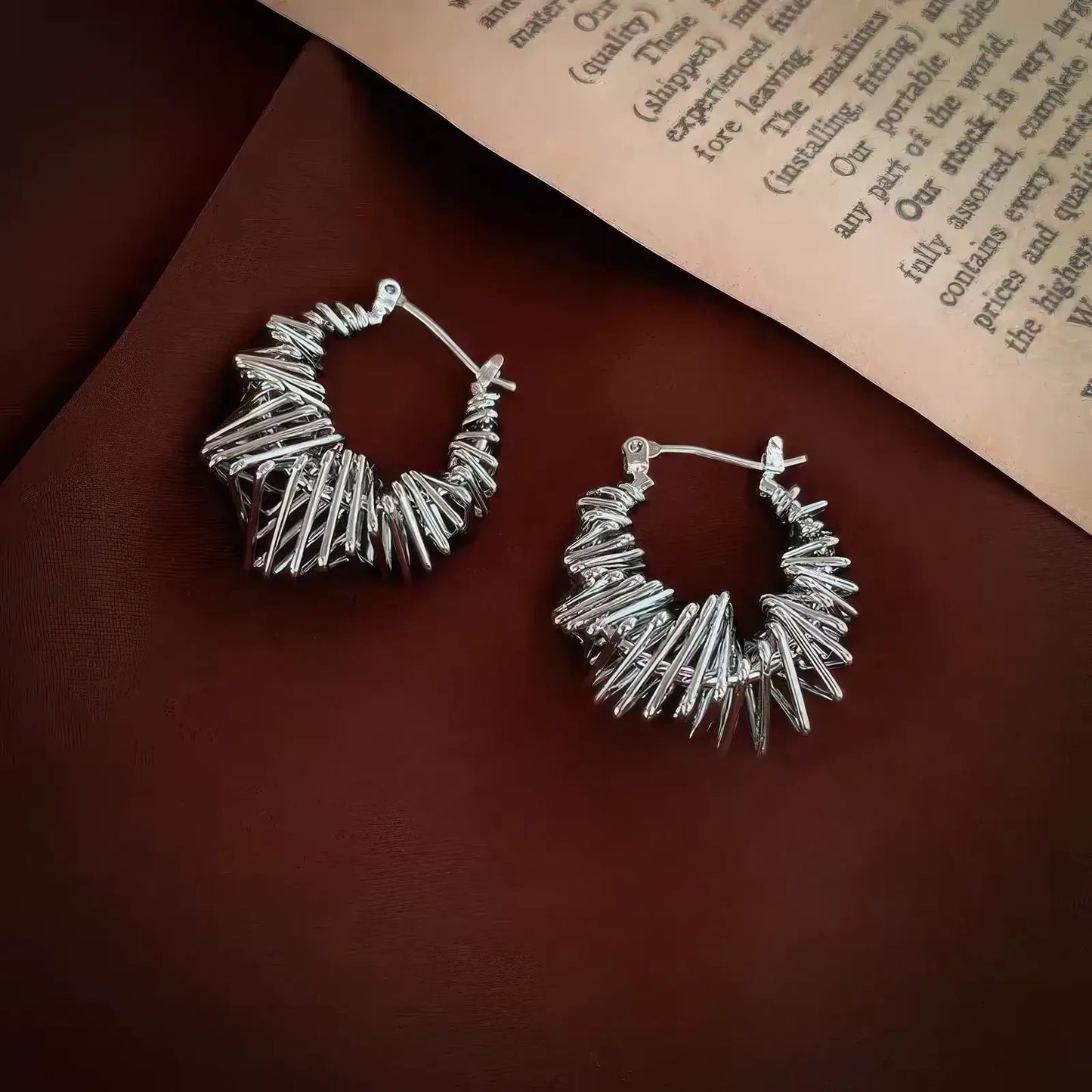  Silver wrapped metal circle earrings displayed on brown fabric, emphasizing the intricate, twisted metal design