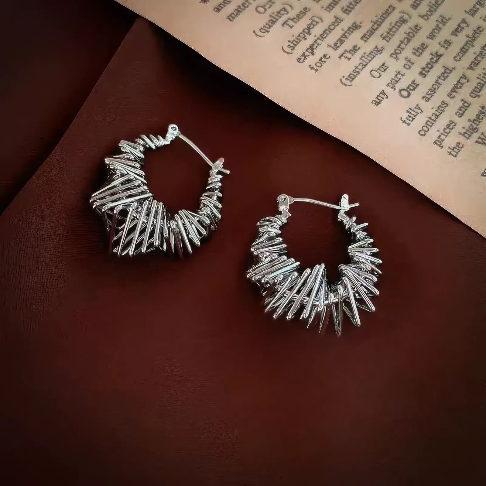  Silver wrapped metal circle earrings displayed on brown fabric, emphasizing the intricate, twisted metal design