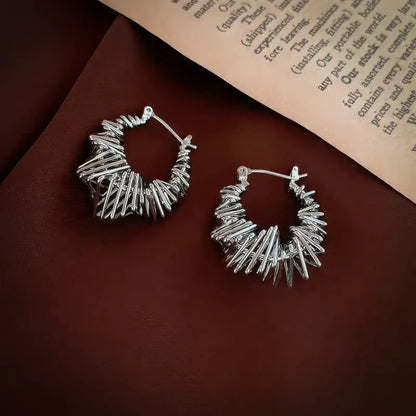  Silver wrapped metal circle earrings displayed on brown fabric, emphasizing the intricate, twisted metal design