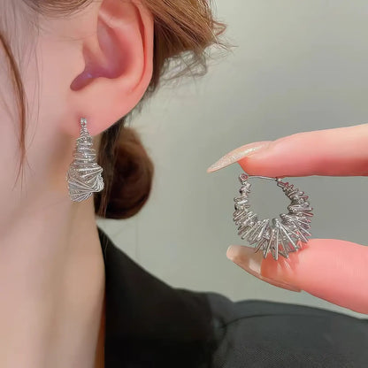 Silver wrapped metal circle earring worn, with hand holding the other earring, highlighting the detailed, twisted structure