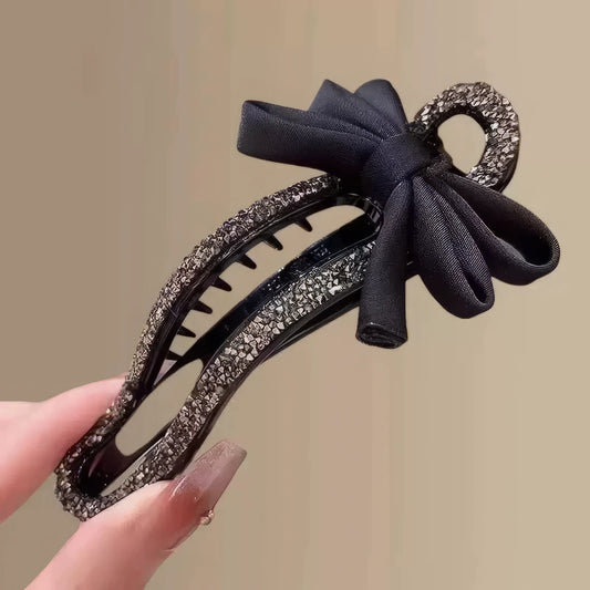 Hand holding black bow rhinestone hair clip, light background