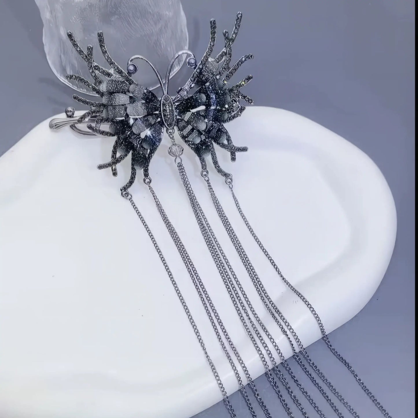 Black butterfly tassel twist clip displayed on a white plate, light background