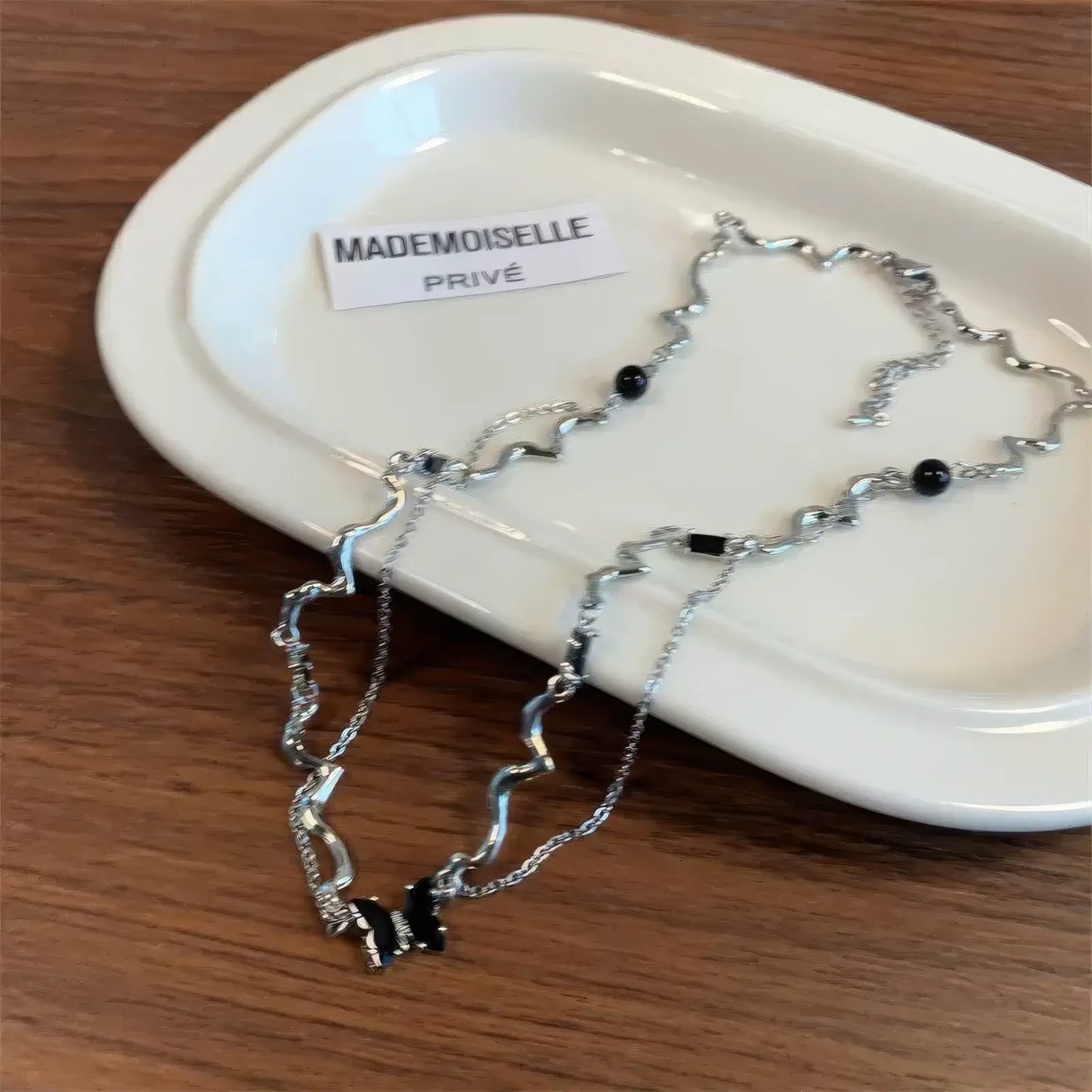 Black zircon butterfly necklace placed on a white tray, emphasizing the brand label "MADEMOISELLE"