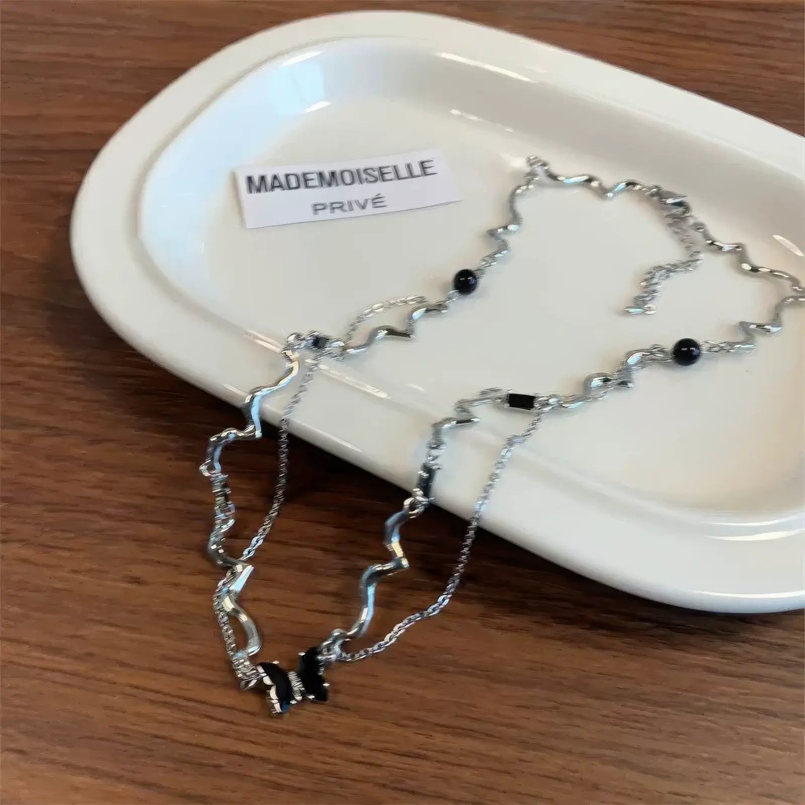 Black zircon butterfly necklace placed on a white tray, emphasizing the brand label "MADEMOISELLE"