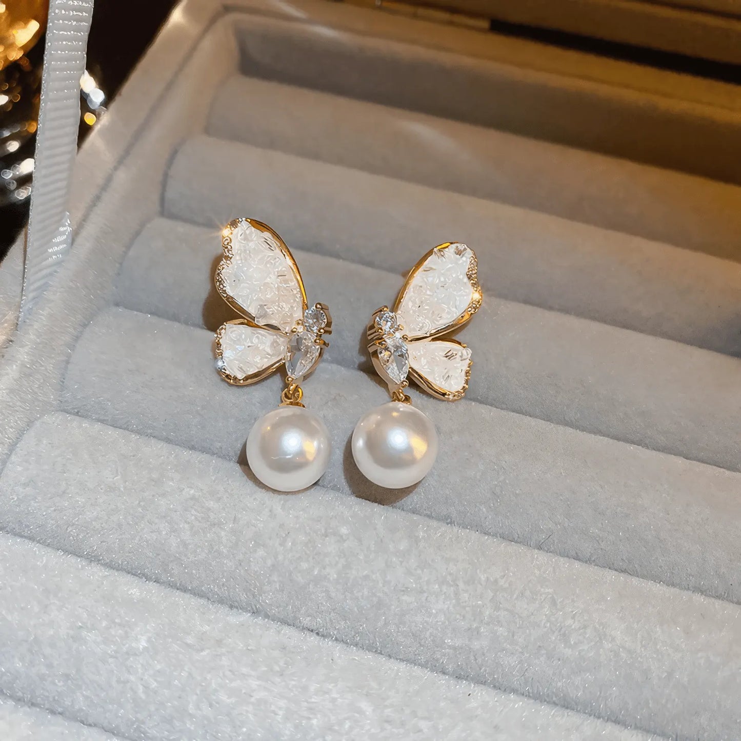 Blue crystal butterfly earrings featuring large pearls on a tray