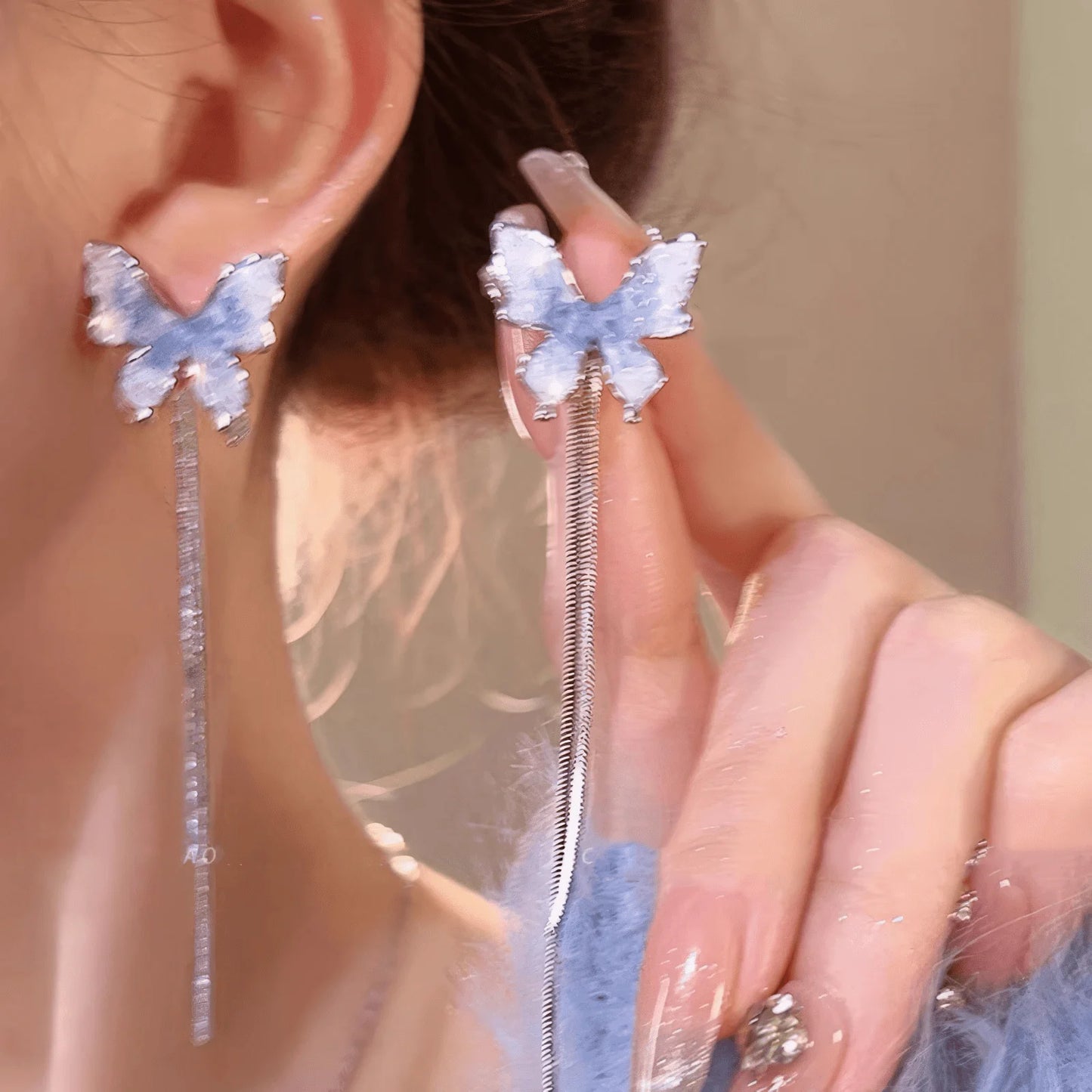 Blue crystal butterfly earrings with tassels being held