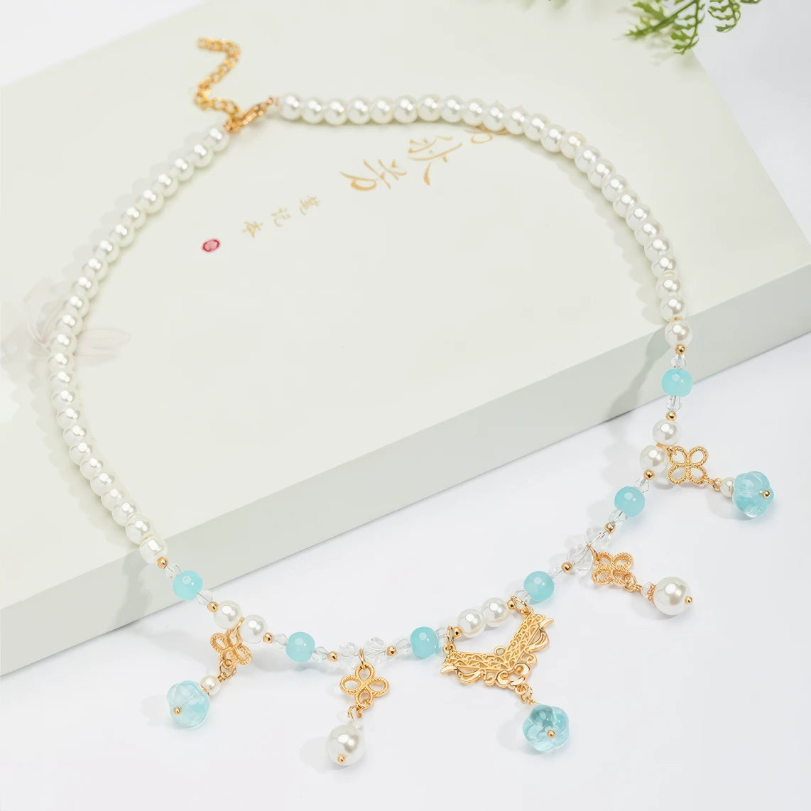 Blue pumpkin bead necklace with pearls and gold details, displayed on white box, light background