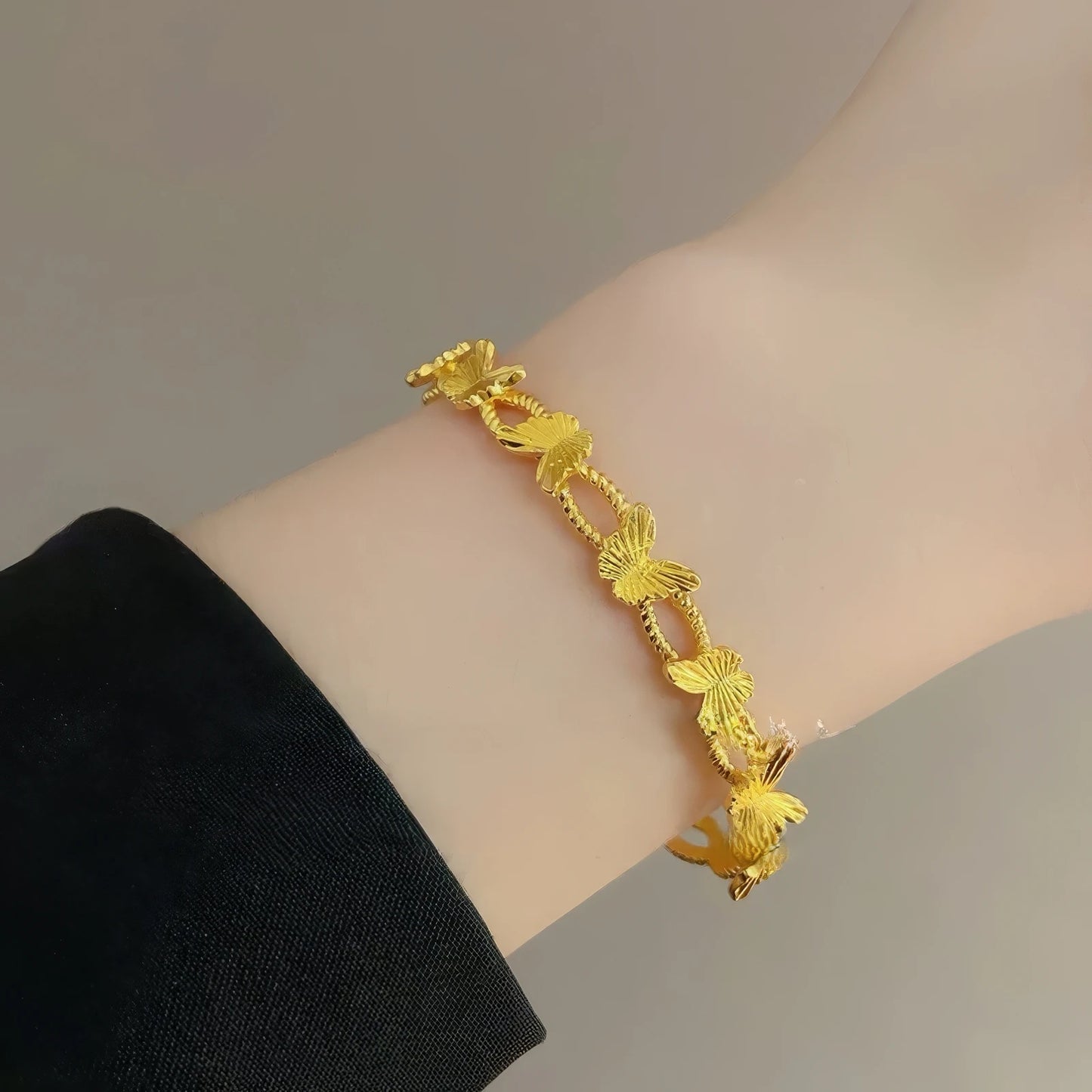 Gold butterfly bracelet worn on wrist, black sleeve in background, emphasizing elegance