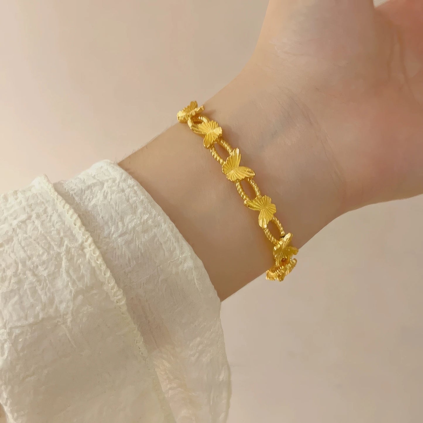 Gold butterfly bracelet worn on wrist, white sleeve in background, highlighting style