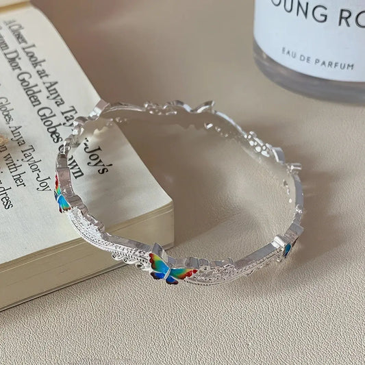 Butterfly enamel oil - drop bangle placed on a book, perfume bottle in background