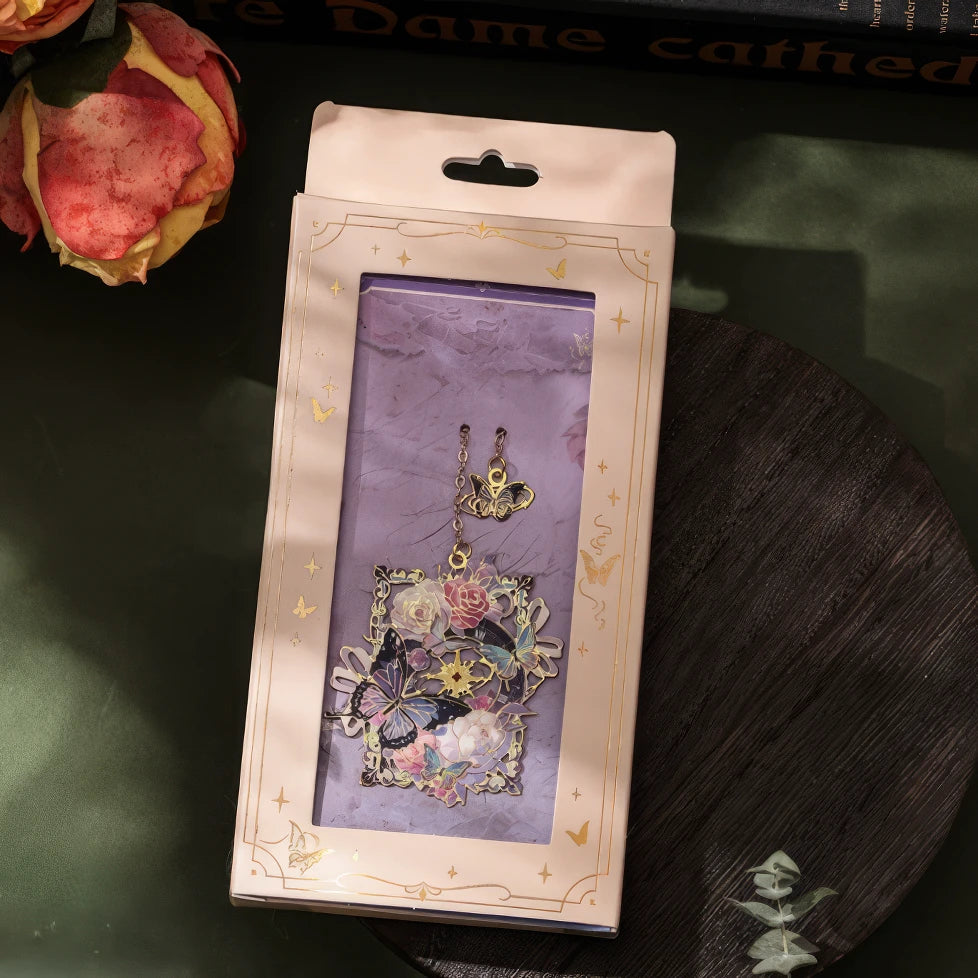 A hand holding a butterfly - shaped metal lattice bookmark, with a table with greenery in the background, realistic product display style, 3:4 ratio