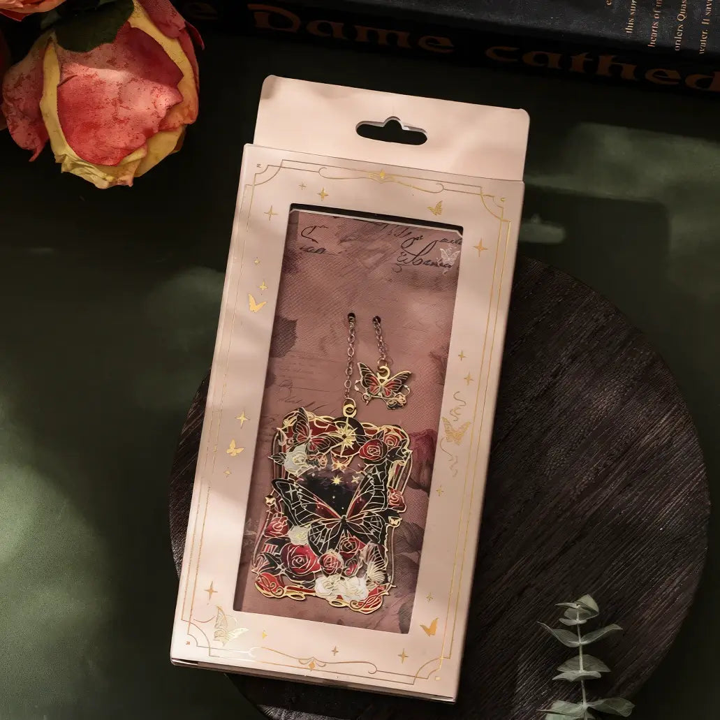 Butterfly - shaped metal lattice bookmark in purple packaging, shown on a table with greenery, realistic product display style, 3:4 ratio