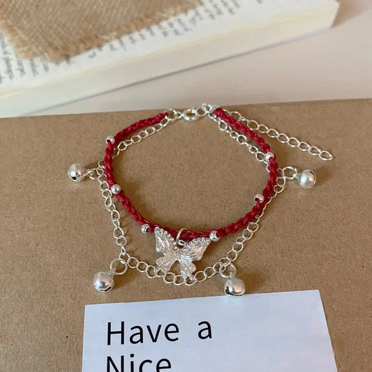 Butterfly red string bell bracelet displayed with “Have a Nice” card, brown surface