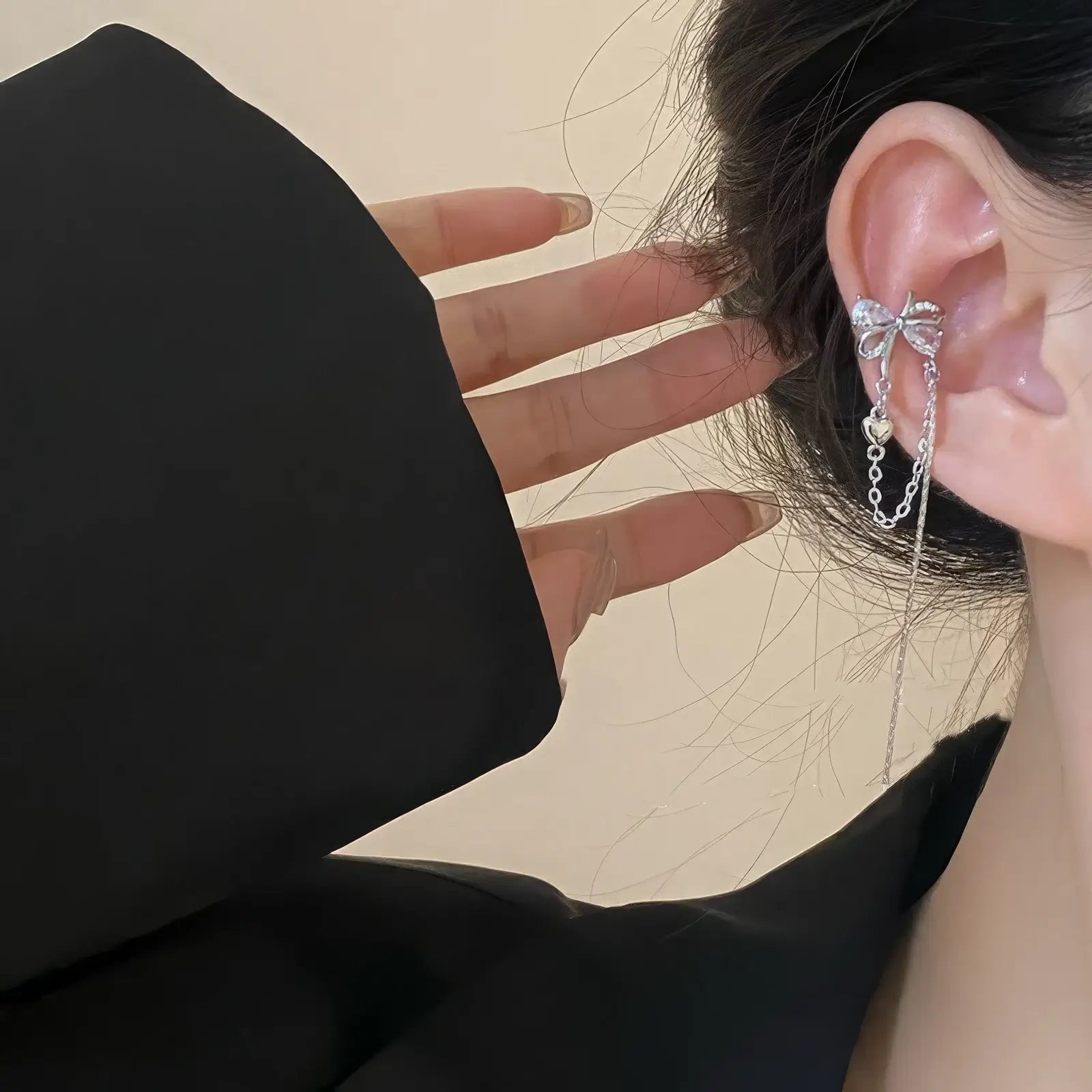 Silver butterfly zircon ear cuff with tassel worn on ear, hand adjusting, black clothing in background
