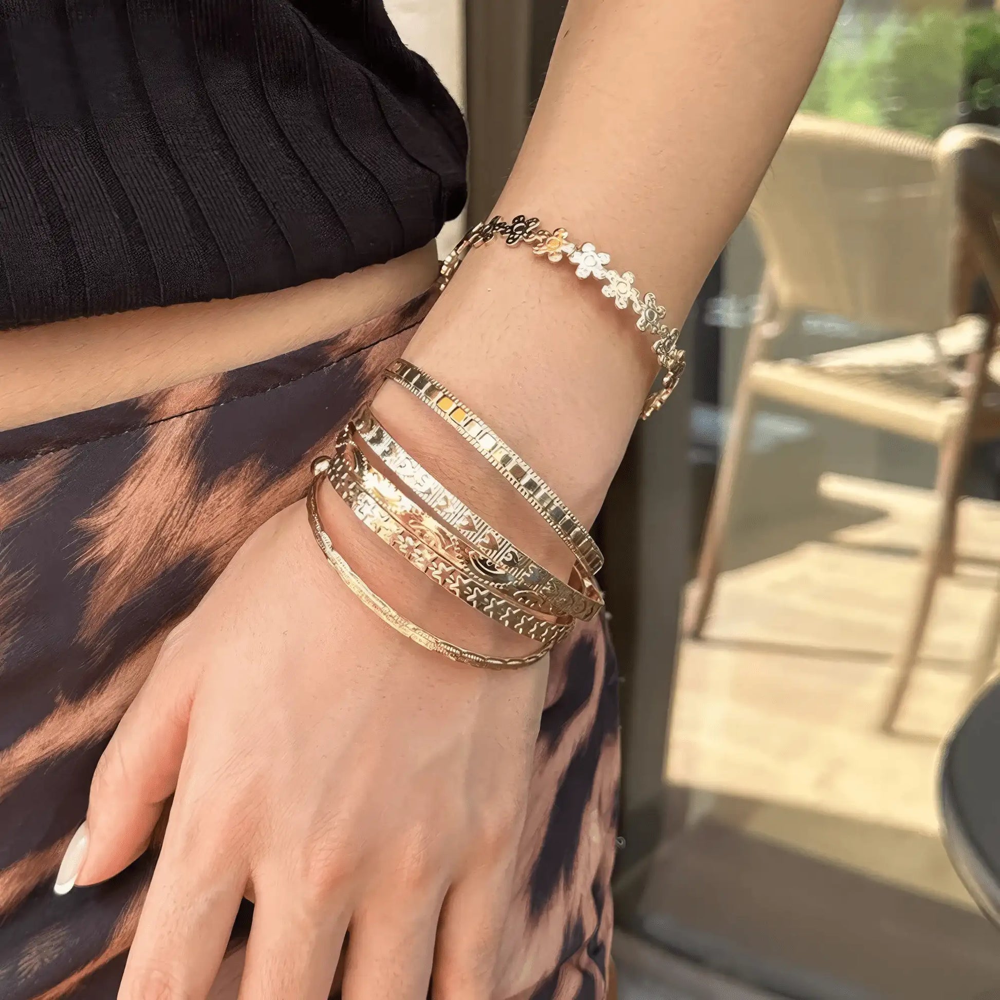 Gold carved pattern flower bangles worn on wrist, emphasizing layering