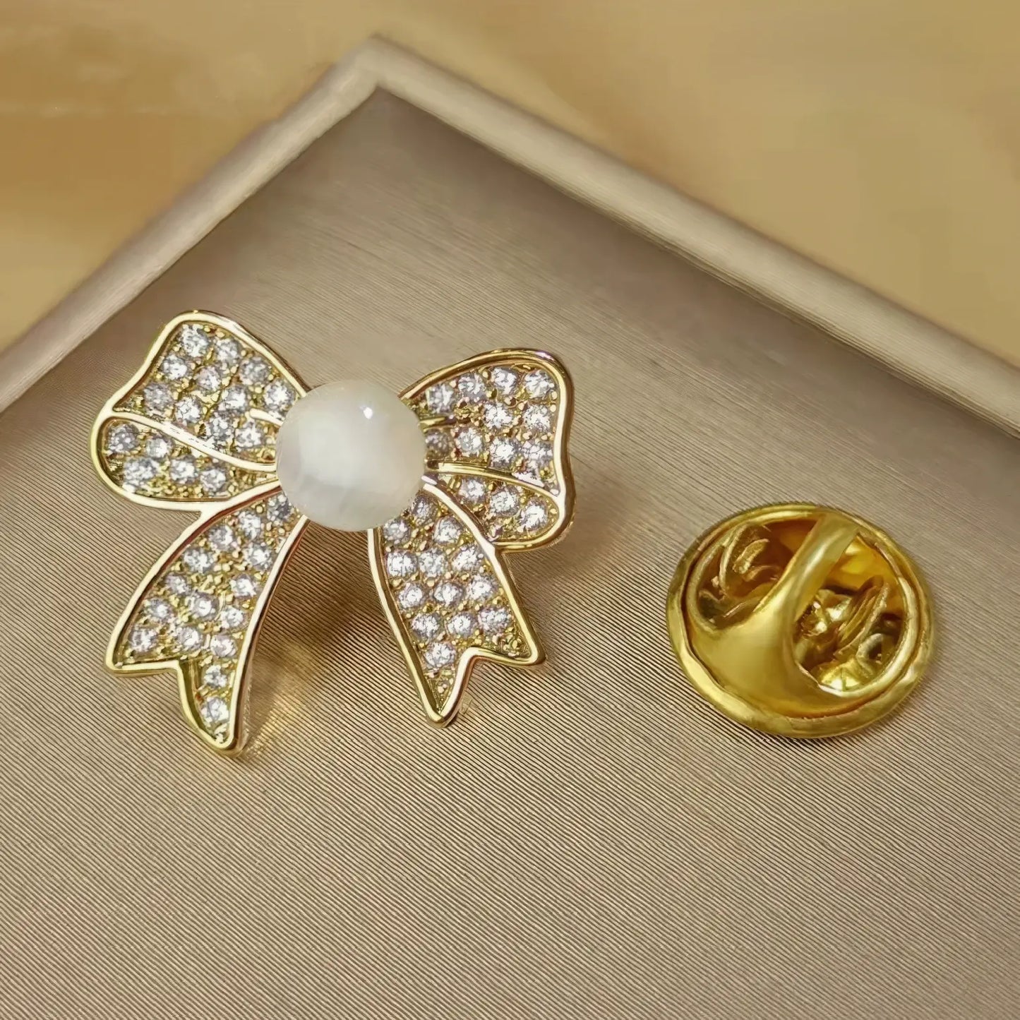 Cat - eye stone brooch with bow design, gold pin backing, displayed on beige pad