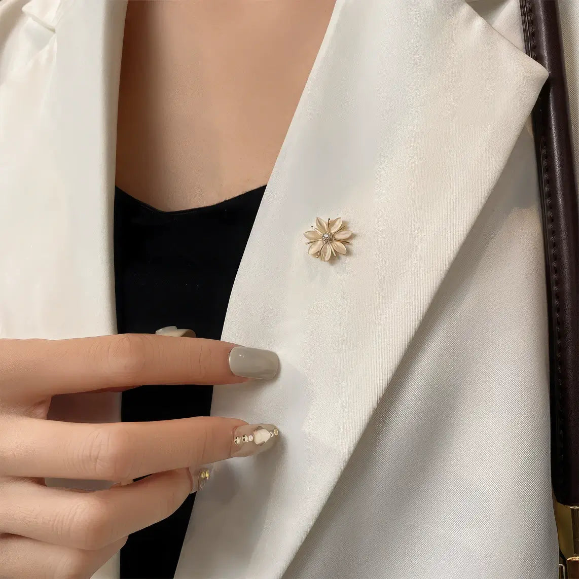 Small cat - eye stone brooch worn on white blazer, hand adjusting, showcasing subtle elegance