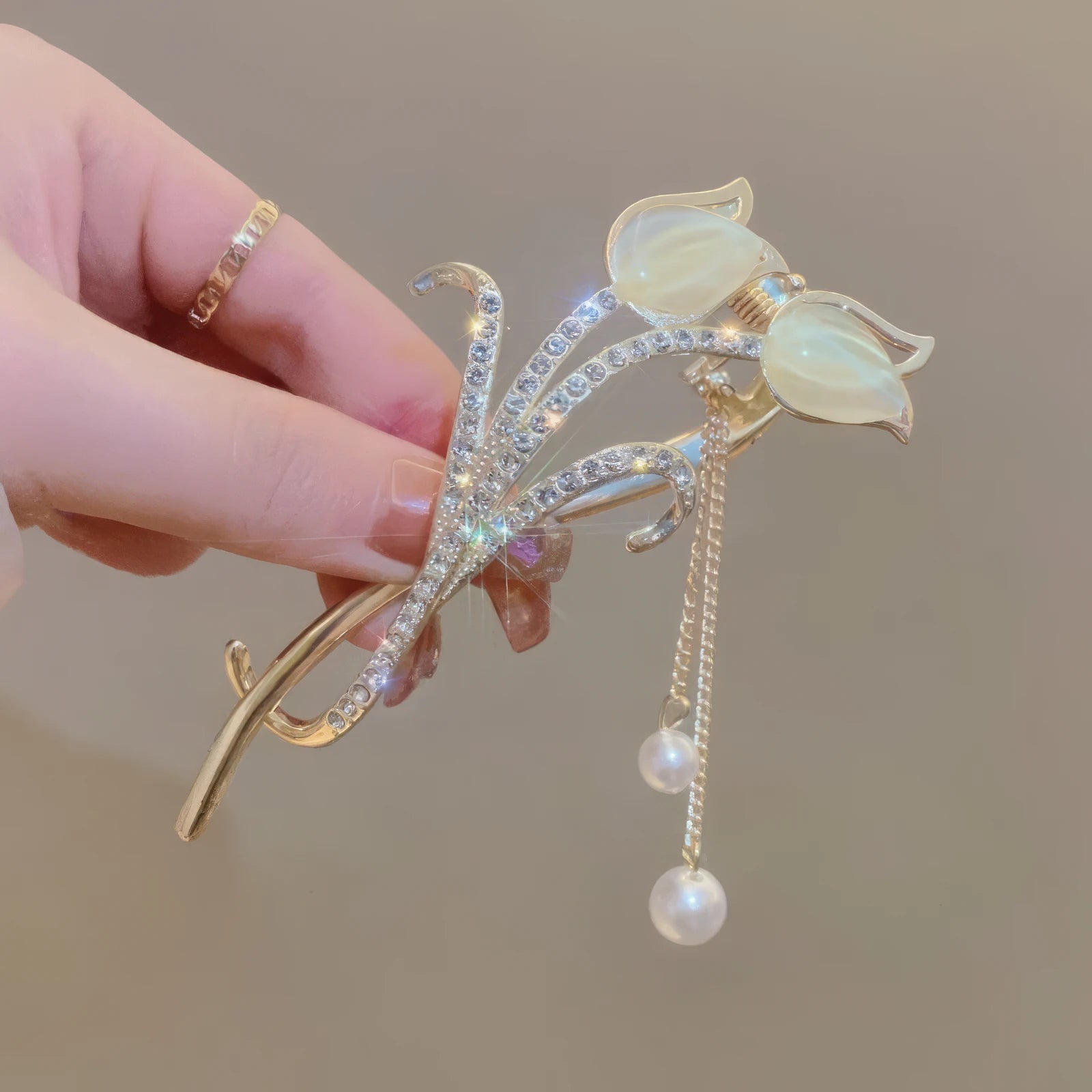 Another view of hand holding white cat - eye stone tulip tassel hair clip