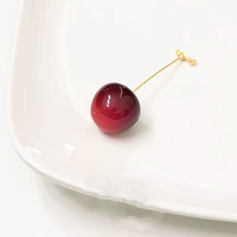 Single dark red cherry - shaped earring, placed on white plate