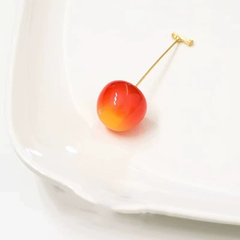 Single gradient (orange to red) cherry - shaped earring, placed on white plate