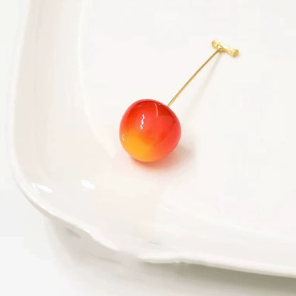 Single gradient (orange to red) cherry - shaped earring, placed on white plate