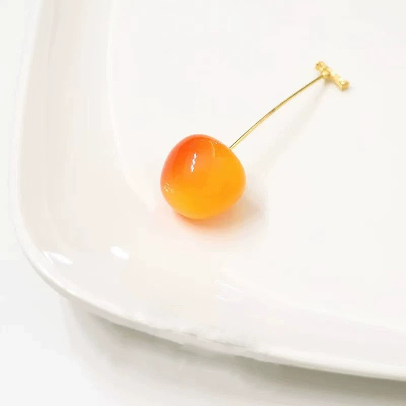 Single orange cherry - shaped earring, placed on white plate