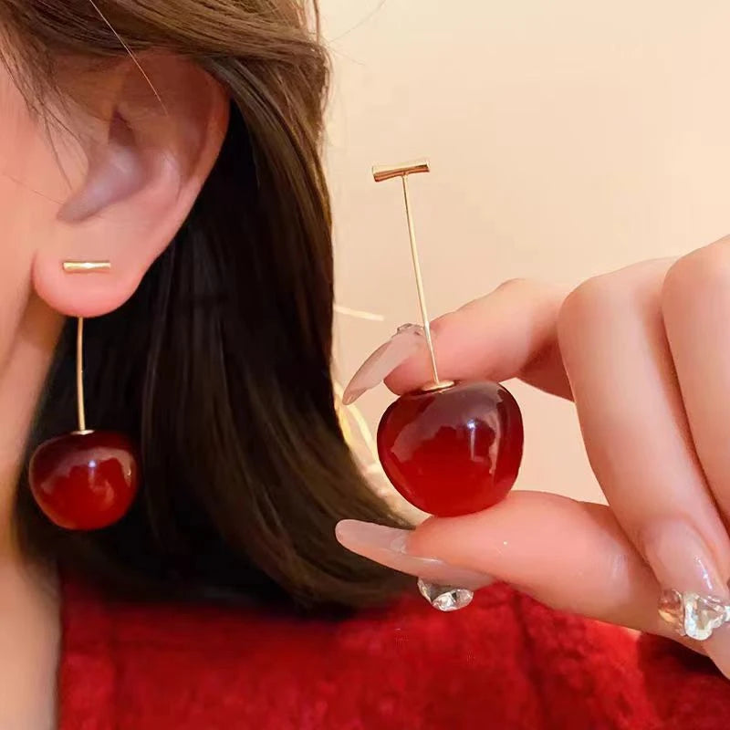 Red cherry - shaped earrings worn on ear, hand adjusting, showcasing style