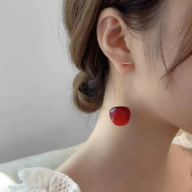 Side view of red cherry - shaped earrings worn on ear, highlighting design