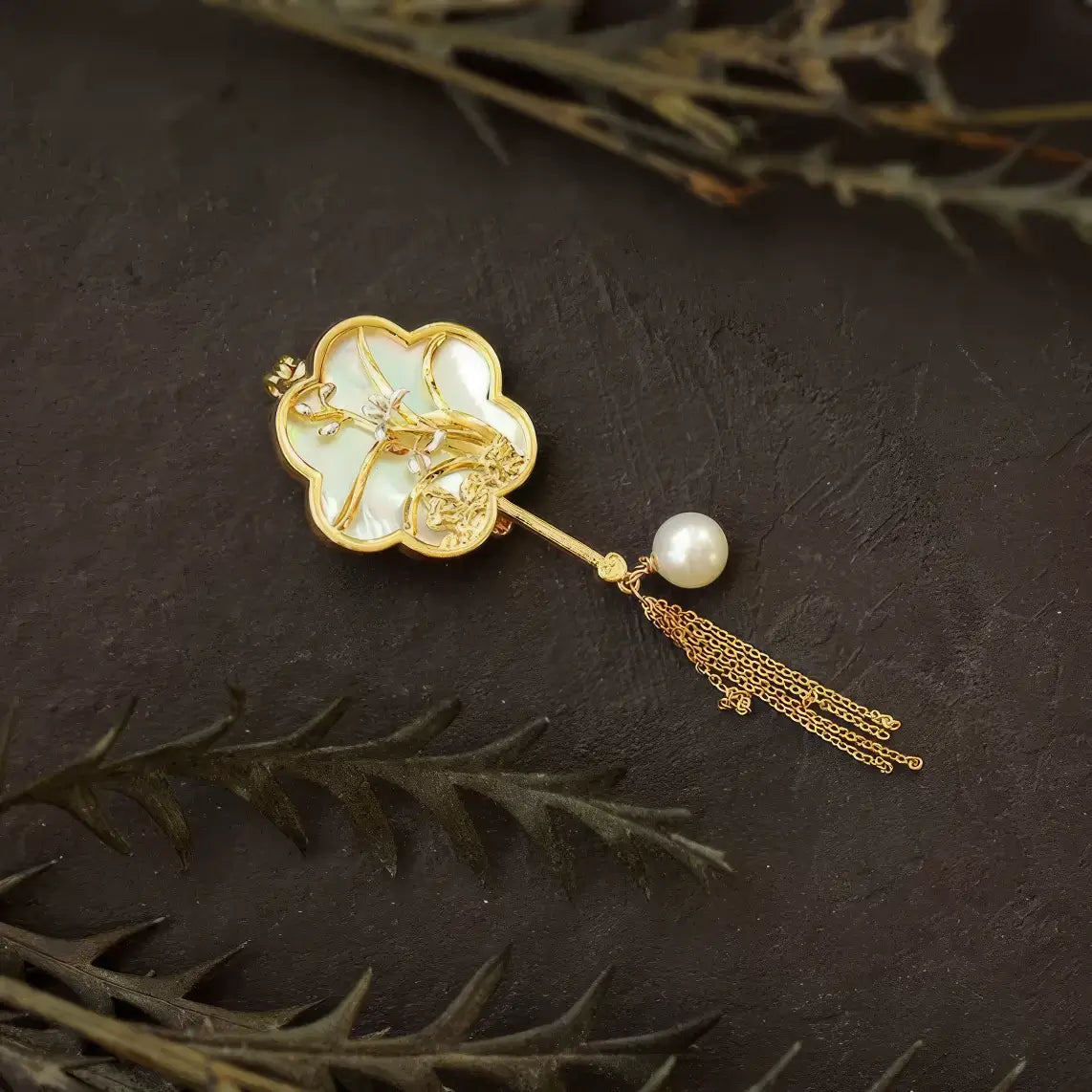 Ivory fan-shaped Chinese-style brooch with pearl inlays and gold tassels, on dark wooden background