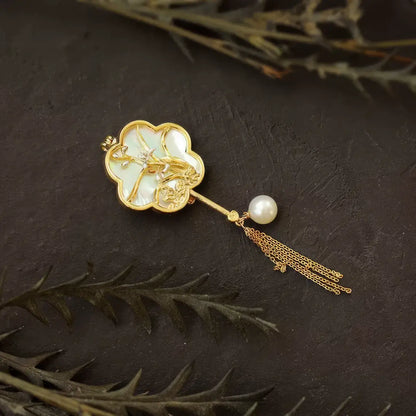 Ivory fan-shaped Chinese-style brooch with pearl inlays and gold tassels, on dark wooden background