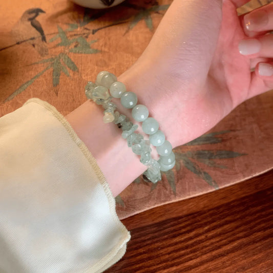 Hands wearing cloud - mountain neo - Chinese beaded bracelets, on a wooden table with bamboo pattern, light background
