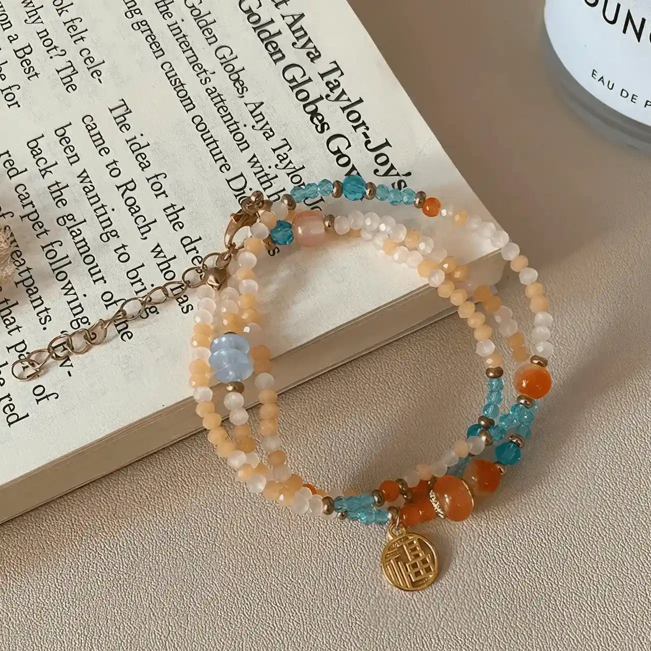 Colorful beaded bracelet with gold pendant, placed on open book, light background
