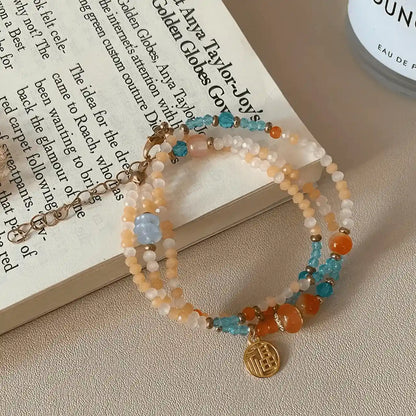 Colorful beaded bracelet with gold pendant, placed on open book, light background