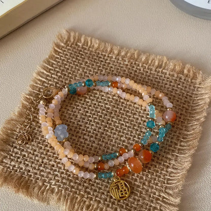 Colorful beaded bracelet with gold pendant, displayed on burlap square, light background