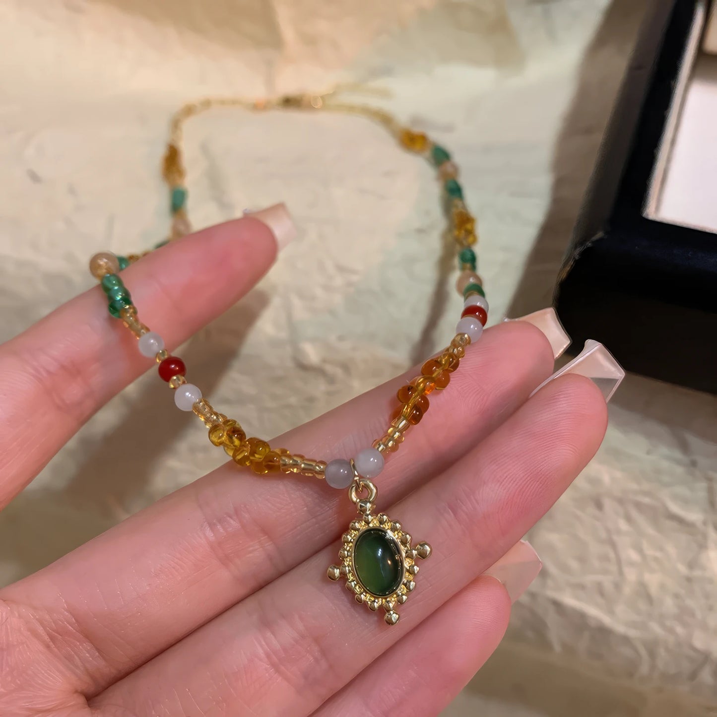 Hand holding colorful beaded pendant necklace, showcasing a green - centered pendant with mixed - color beads