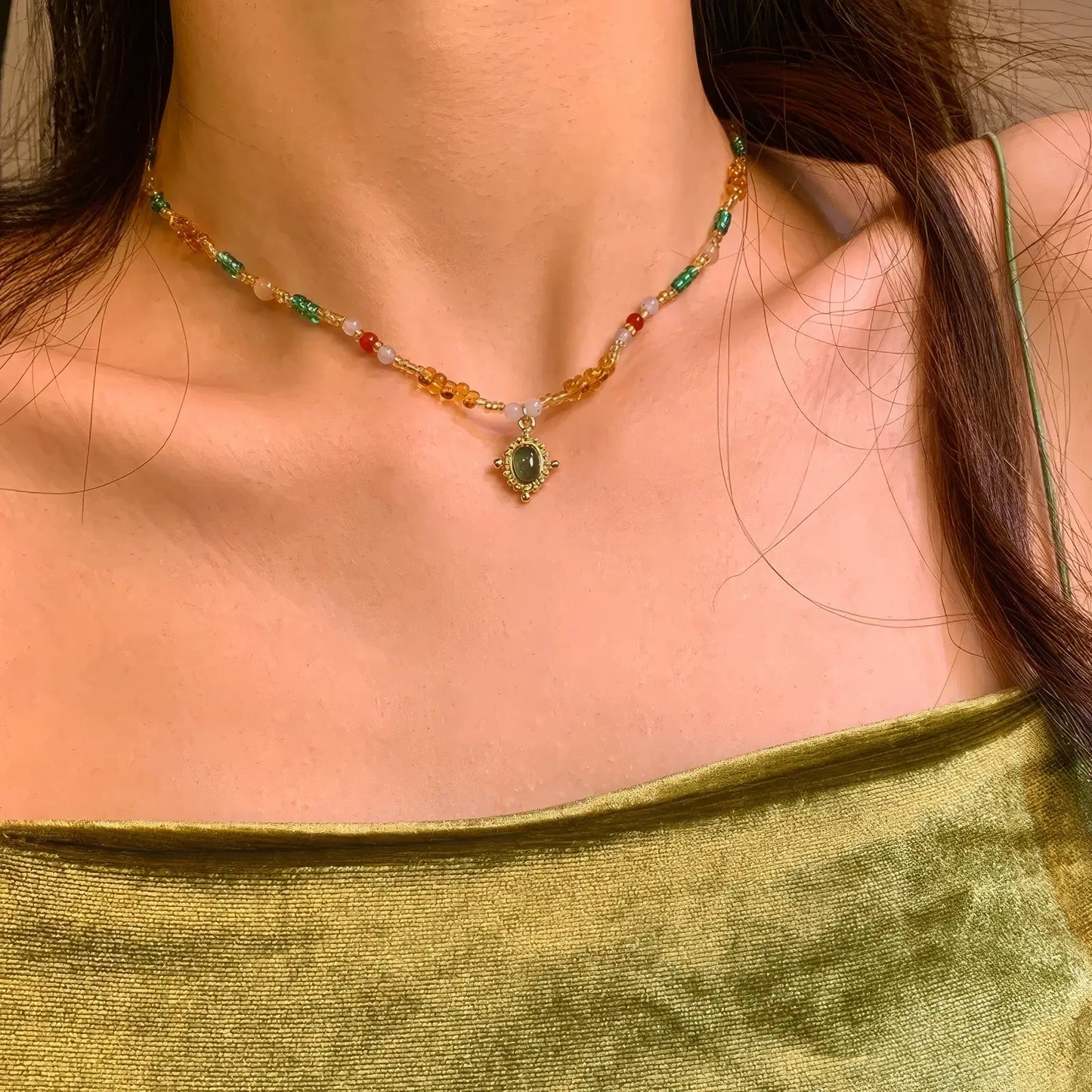 Colorful beaded pendant necklace worn, paired with a green garment, highlighting the necklace's colors