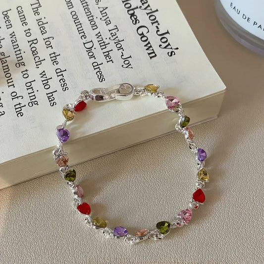 Colorful zircon heart bracelet placed on an open book, beige background
