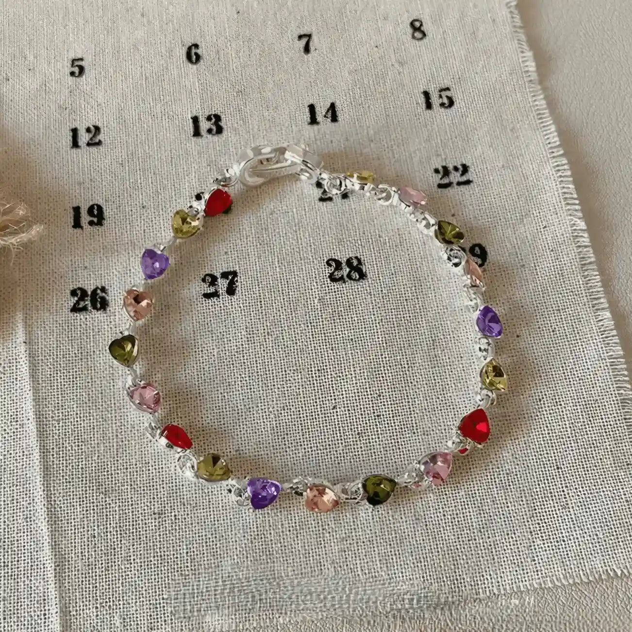 Colorful zircon heart bracelet displayed on a calendar - printed fabric, beige background