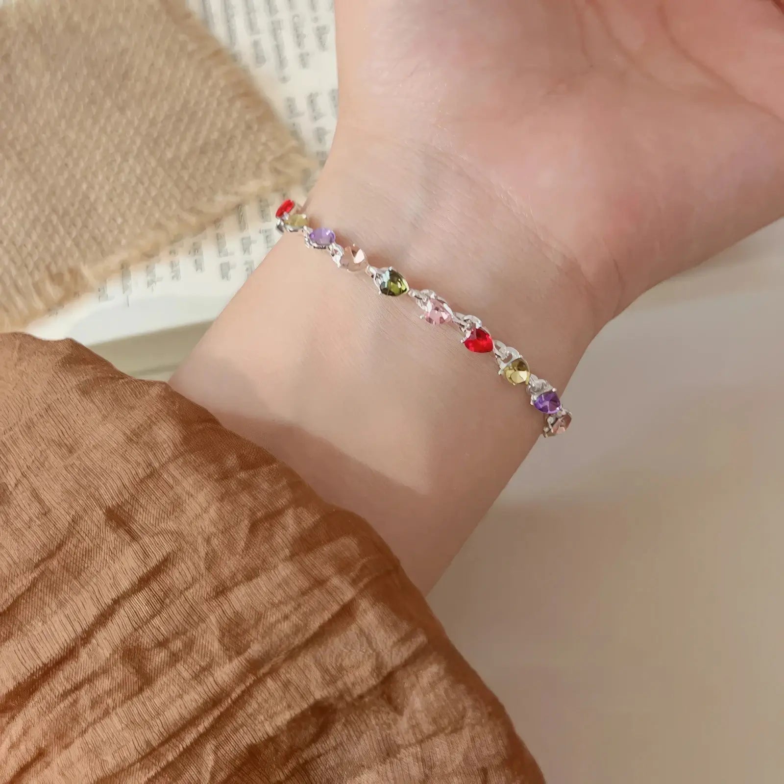 Colorful zircon heart bracelet worn on a wrist, brown sleeve background