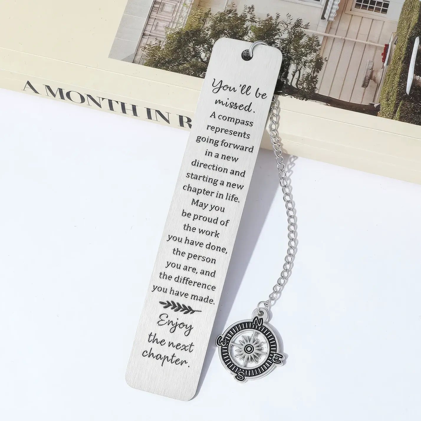 Compass metal bookmark with chain, placed in open book, light background