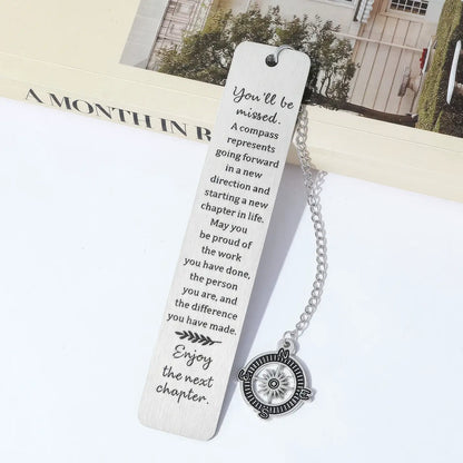 Compass metal bookmark with chain, placed in open book, light background
