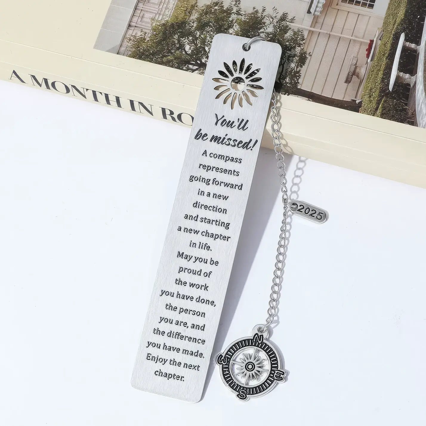 Compass metal bookmark with chain, placed in open book, light background